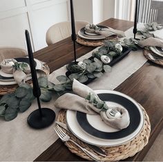 the table is set with black and white plates, silverware, eucalyptus leaves and candlesticks