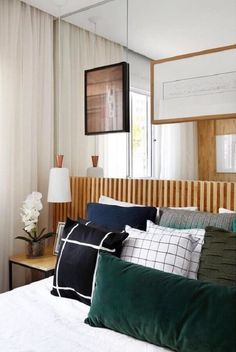 a bed topped with lots of pillows next to a window filled with white and green curtains