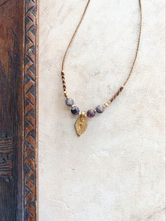 a necklace with beads and a gold leaf charm hanging from it's side on a white surface