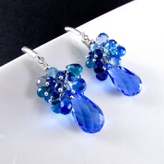 "Stunning cobalt blue lab created topaz dangle below a generous cluster of sparkling briolettes consisting of turquoise blue, navy blue, peacock green and sky blue quartz. I have used all sterling silver to keep them fresh. The gems are topped off with another blue topaz gem and a sterling silver bead. The blue topaz measure 20x11mm. The total earring length is 2 1/8\" (54mm.) from the top of the lever back ear wires." Blue Briolette Gemstone Earrings, Blue Faceted Drop Earrings, Blue Sapphire Cluster Earrings For Gift, Blue Gemstone Accented Drop Earrings, Blue Drop Earrings With Gemstone Accents, Blue Gemstone Cluster Earrings As Gift, Blue Gemstone Cluster Earrings For Gift, Blue Peacock, Earrings Handmade Dangle