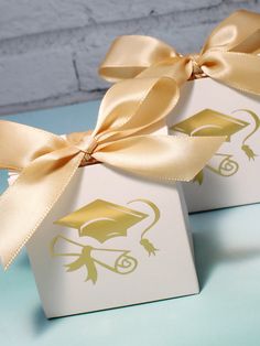 two white boxes with gold ribbons and graduation caps on them are sitting on a table