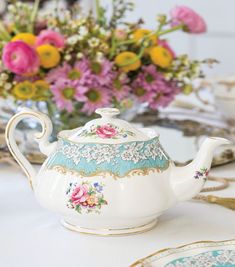 a white table topped with a tea pot filled with lots of pink and yellow flowers