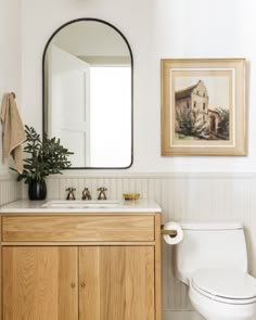 a white toilet sitting next to a wooden cabinet in a bathroom under a large mirror