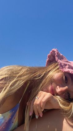 a woman laying on the beach with her hair blowing in the wind and wearing a pink hat