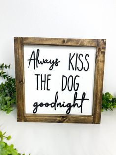 a sign that says, always kiss the dog good night on it next to some plants