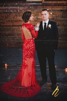 a man and woman standing next to each other in front of a wooden wall with candles