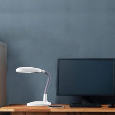 a desk with a monitor, keyboard and mouse on it next to a wall mounted lamp