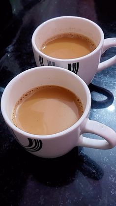 two white cups filled with liquid sitting on top of a black counter next to each other