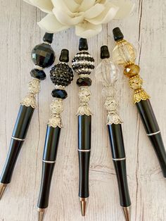 four pens are lined up next to a flower on a white wooden surface with beads