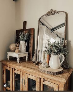 a wooden table topped with a white vase filled with flowers and a mirror on top of it