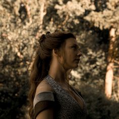 a woman standing in front of trees with her hair pulled back and looking off to the side