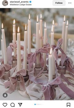 a table topped with lots of white candles covered in pink satin ribbons and bowknots