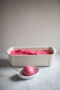 a scoop of pink ice cream in a white bowl with a spoon next to it