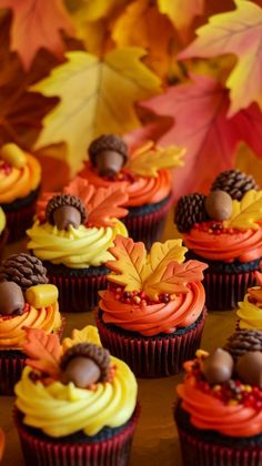 cupcakes decorated with leaves and acorns are displayed on a table in front of autumn leaves