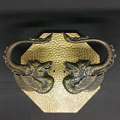 two metal dragon bracelets on a black surface with gold and silver accents, one in the shape of a shield