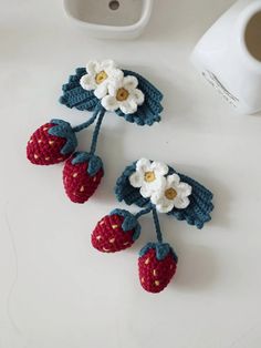 two crocheted strawberries with flowers on them next to a cup of coffee