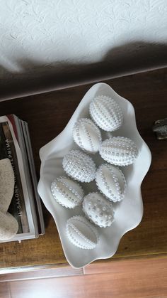 a white bowl filled with lots of fake eggs on top of a table next to a book