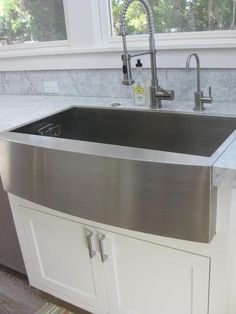 a stainless steel sink in a kitchen with marble counter tops and white cabinetry next to a window