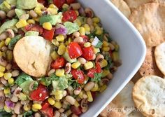 a white bowl filled with corn, tomatoes and avocado next to tortilla chips