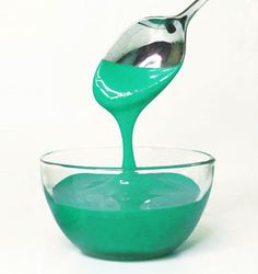 a spoon is pouring green liquid into a bowl