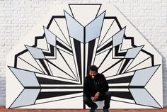 a man squatting in front of a large piece of art