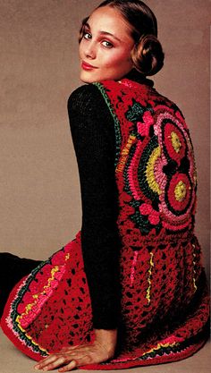 a woman sitting on the ground wearing a red and black dress with an intricate design