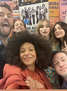 a group of people standing next to each other in front of posters on the wall