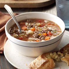 a bowl of soup on a plate next to a piece of bread and glass of water