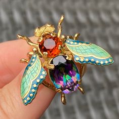 "A beautifully designed vintage fly or insect pin crafted in 18K yellow gold showcasing a vibrant mystic topaz and fiery orange citrine. The wings have been enameled with an unusual combination of minty green and teal green hues. This piece is larger in scale, measuring 1.2 inches long by 1.4 inches wide. The back of the pin is stamped \"750\" for 18K gold purity marks. The pin stem itself has likely been stamped \"K18\" along with Italian hallmarks for 18K gold purity, while the pin holder/lock Fly Insect, Stacked Diamond Bands, Orange Citrine, Pin Holder, Wedding Rings Photos, Bee Brooch, Insect Jewelry, Minty Green, Gold Pin