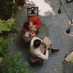 two people sitting at an outdoor table with umbrellas and chairs around them, looking down on the ground