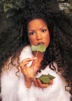 a woman with long curly hair holding a leaf