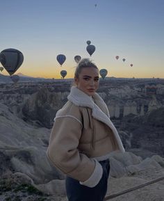 a woman standing on top of a hill next to hot air balloons