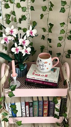 a pink shelf with books and flowers on it