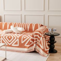 a living room with a couch covered in an orange and white blanket next to a table