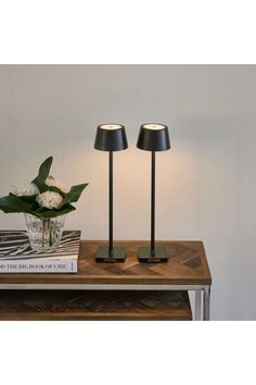 two black lamps sitting on top of a wooden table next to a vase with flowers