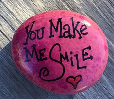 a pink rock with the words you make me smile written on it, sitting on a wooden surface