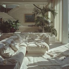 a living room filled with lots of white furniture next to tall windows and potted plants