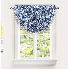 a blue and white window valance with pom poms on the bottom, in front of an open window