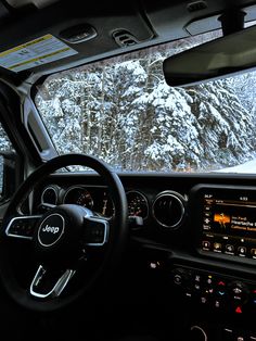 the interior of a vehicle with snow covered mountains in the background and dashboard lights on