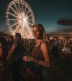 a woman standing in front of a ferris wheel at night with other people around her