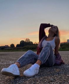 a woman sitting on the ground with her head in her hair and wearing white sneakers