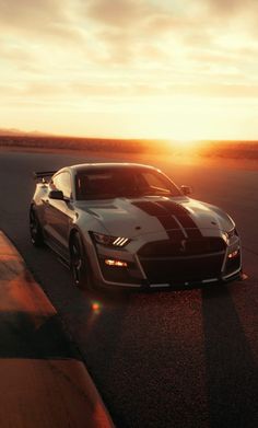 a sports car driving down the road at sunset