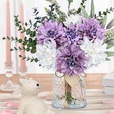 a vase filled with purple and white flowers next to a teddy bear on a table