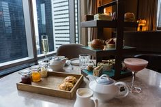 a table with tea, pastries and drinks on it in front of a window