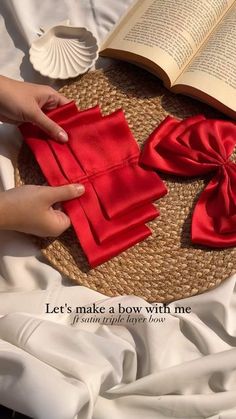 a person is making a bow with red cloth on top of a round mat that has an open book and seashell in the background