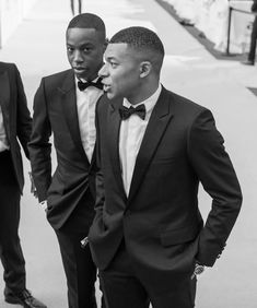 two men in tuxedos standing next to each other on the sidewalk, one wearing a bow tie