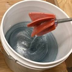 a red spatula sticking out of a bucket filled with blue liquid on top of a wooden table