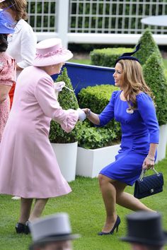 two women in pink dresses and hats shaking hands