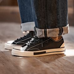 a person standing on top of a wooden floor wearing black converse shoes with white laces