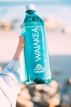 a person holding up a water bottle in front of the ocean